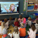 Photo of MBHI Educator Carolyn holding a leaf insect on a screen while children sit on the floor and learn.