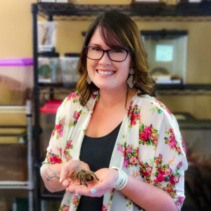 Photo of MBHI employee, Morgan McNeill, smiling at the camera while holding the tarantula, Rosie.