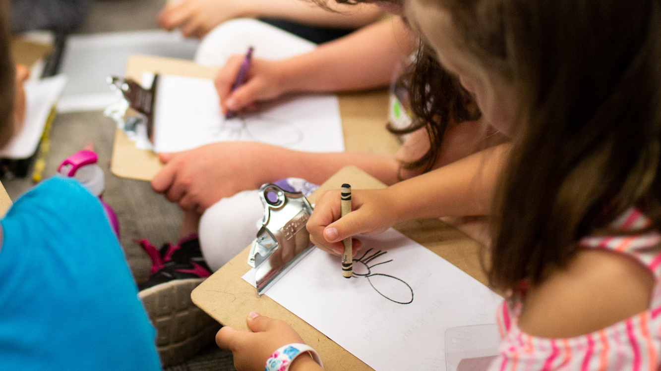 Closeup of a girl drawing a spider on a clipboard.